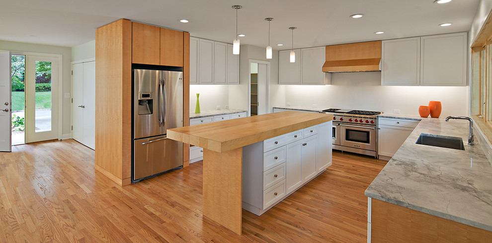 Idéer för ett modernt kök, med en undermonterad diskho, skåp i shakerstil, vita skåp, marmorbänkskiva, rostfria vitvaror, vitt stänkskydd, ljust trägolv, en köksö och beiget golv