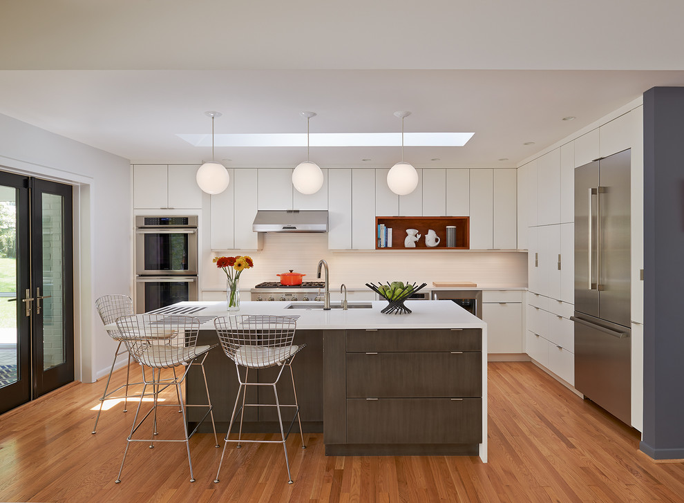 Example of a mid-sized 1960s l-shaped light wood floor and beige floor open concept kitchen design in DC Metro with flat-panel cabinets, white cabinets, an island, quartz countertops, white backsplash, ceramic backsplash, stainless steel appliances and an undermount sink