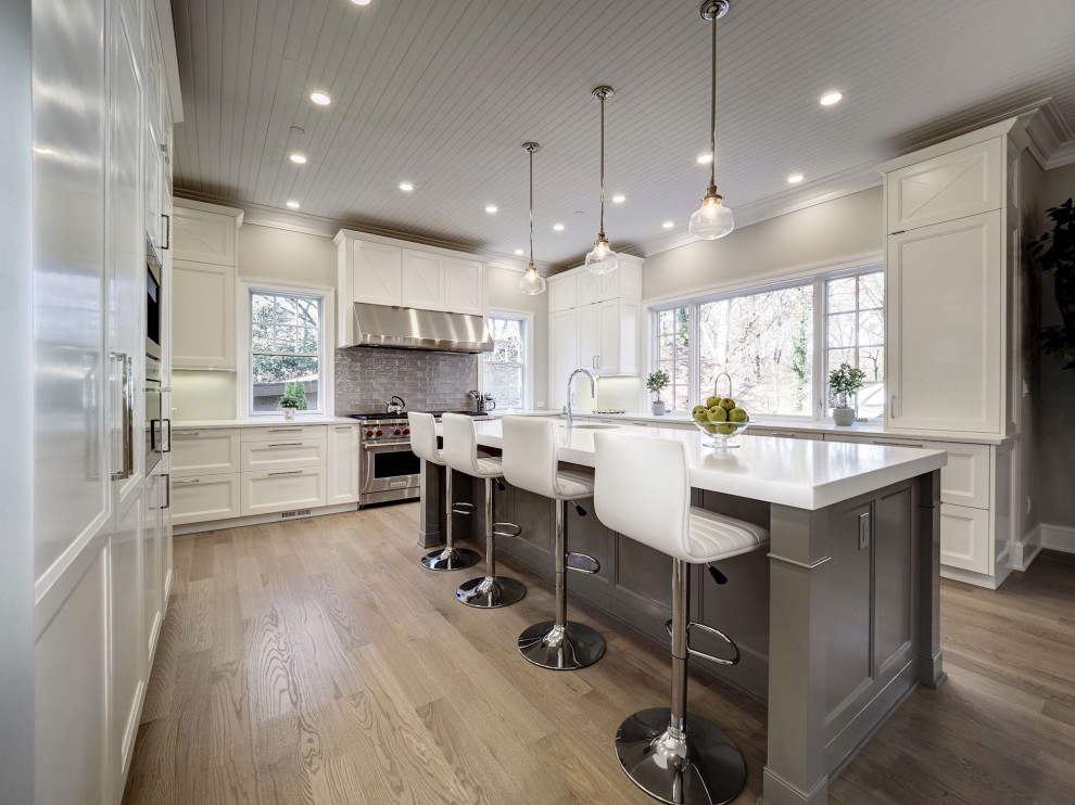Exempel på ett stort klassiskt vit vitt u-kök, med en undermonterad diskho, skåp i shakerstil, vita skåp, grått stänkskydd, rostfria vitvaror, mellanmörkt trägolv, en köksö och beiget golv
