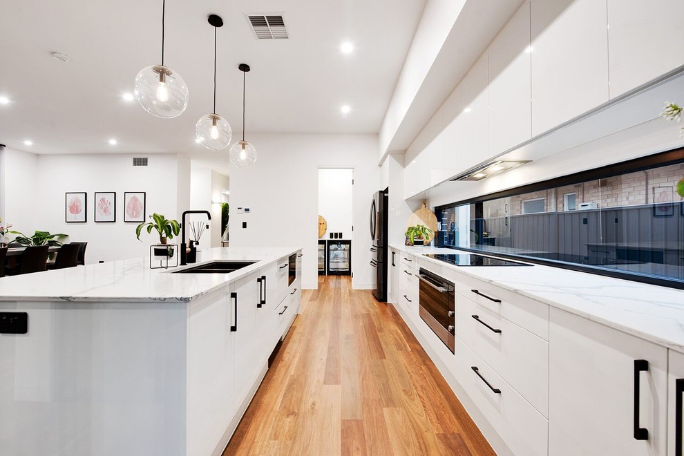 アデレードにある高級な中くらいなモダンスタイルのおしゃれなキッチン (ダブルシンク、白いキャビネット、黒い調理設備、無垢フローリング、茶色い床、白いキッチンカウンター) の写真