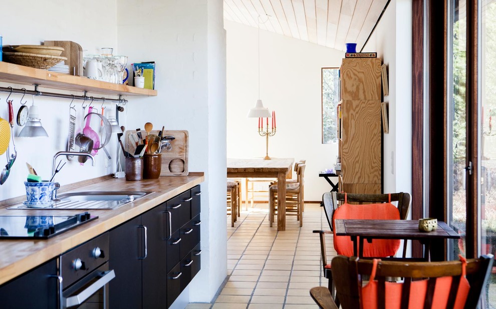 コペンハーゲンにあるお手頃価格の中くらいな北欧スタイルのおしゃれなキッチン (ドロップインシンク、フラットパネル扉のキャビネット、黒いキャビネット、木材カウンター、白いキッチンパネル、テラコッタタイルの床、アイランドなし、シルバーの調理設備) の写真