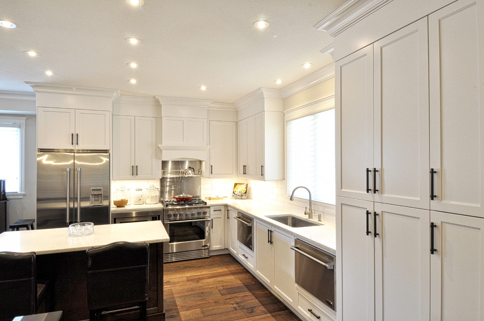 Medium sized traditional l-shaped open plan kitchen in Vancouver with a submerged sink, recessed-panel cabinets, white cabinets, white splashback, stainless steel appliances, medium hardwood flooring and an island.