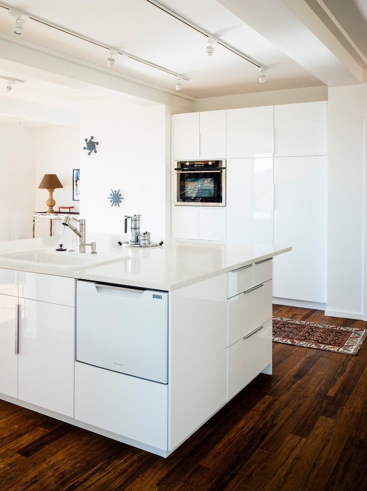 Diseño de cocina contemporánea de tamaño medio con fregadero encastrado, armarios con paneles lisos, puertas de armario blancas, suelo de madera oscura y una isla