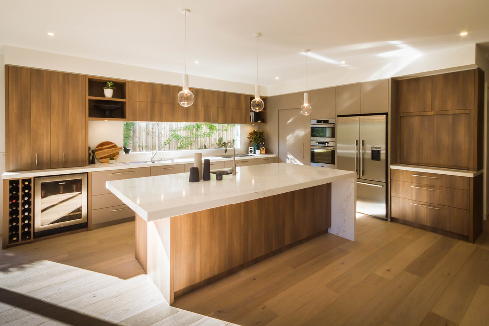 Bild på ett stort funkis kök, med en undermonterad diskho, bänkskiva i kvarts, vitt stänkskydd, stänkskydd i sten, rostfria vitvaror, mellanmörkt trägolv och en köksö