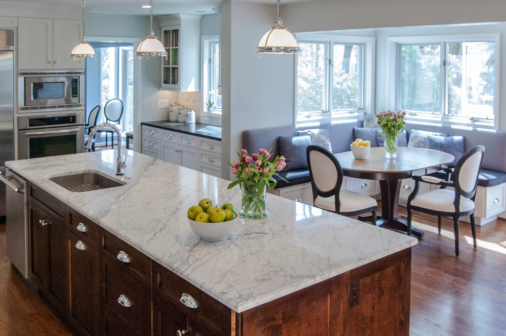 Example of a large transitional l-shaped medium tone wood floor eat-in kitchen design in Philadelphia with an undermount sink, shaker cabinets, white cabinets, granite countertops, white backsplash, stone tile backsplash, stainless steel appliances and an island