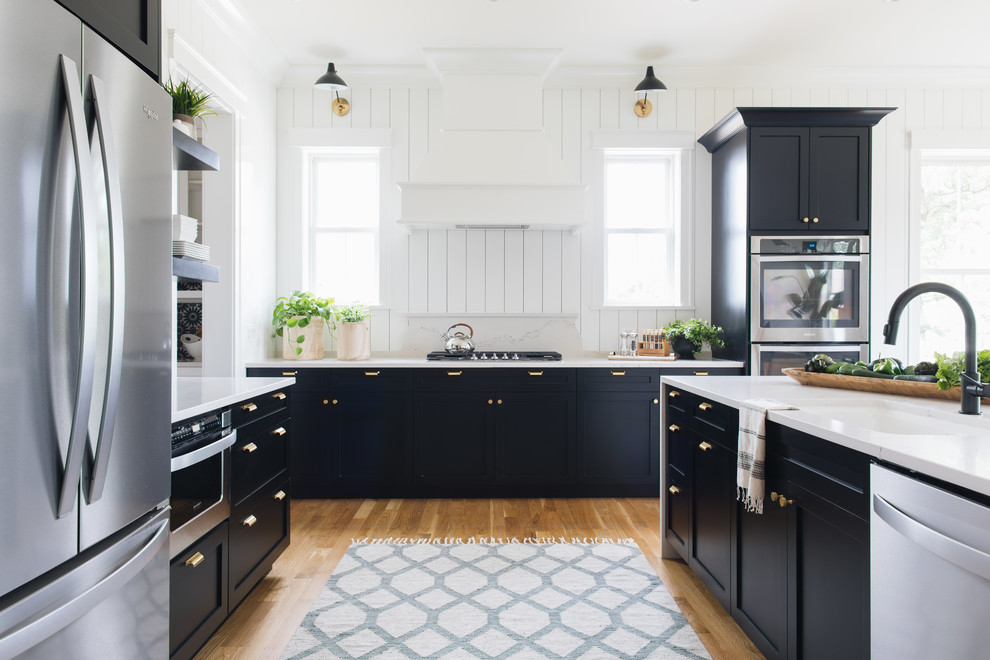 Inspiration for a rural l-shaped kitchen in Chicago with a submerged sink, recessed-panel cabinets, black cabinets, white splashback, stainless steel appliances, medium hardwood flooring, an island, brown floors and white worktops.