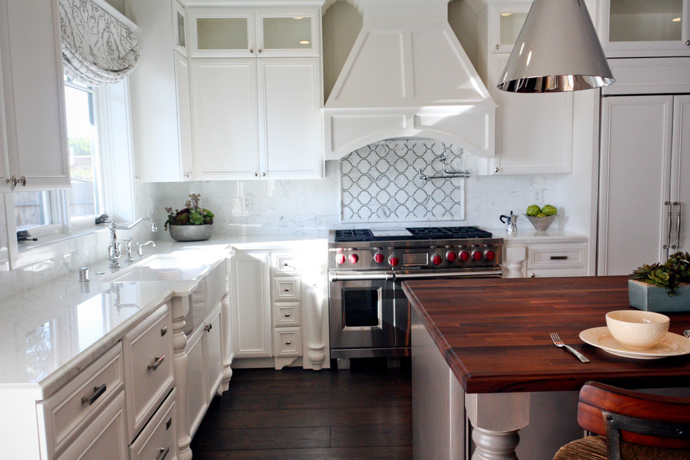 Example of a mid-sized cottage l-shaped dark wood floor kitchen design in Los Angeles with a farmhouse sink, beaded inset cabinets, white cabinets, wood countertops, white backsplash, stainless steel appliances and an island