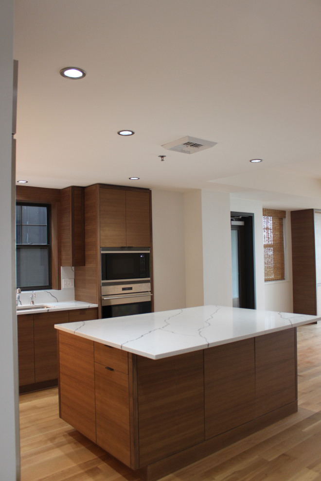Photo of a medium sized contemporary l-shaped open plan kitchen in Portland with a submerged sink, flat-panel cabinets, medium wood cabinets, engineered stone countertops, white splashback, engineered quartz splashback, stainless steel appliances, light hardwood flooring, an island, beige floors and white worktops.