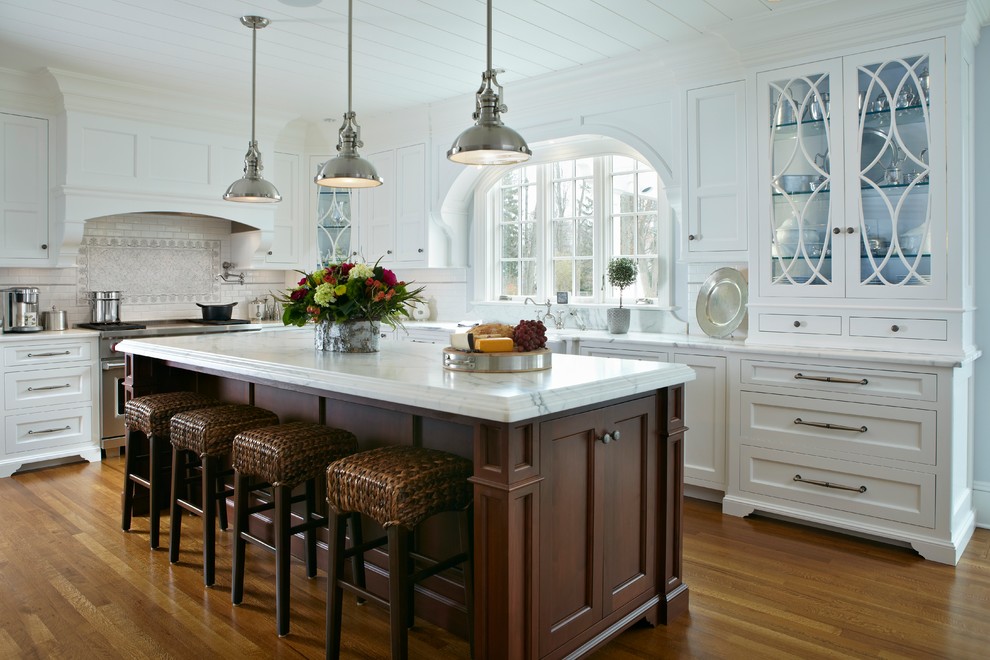 Klassische Küche in L-Form mit Landhausspüle, Schrankfronten im Shaker-Stil, weißen Schränken, Küchenrückwand in Weiß, Küchengeräten aus Edelstahl, braunem Holzboden und Kücheninsel in New York