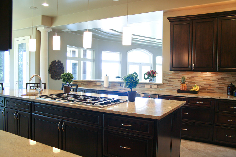 Klassisk inredning av ett stort kök, med en undermonterad diskho, luckor med upphöjd panel, skåp i mörkt trä, granitbänkskiva, flerfärgad stänkskydd, stänkskydd i glaskakel, rostfria vitvaror, travertin golv och en köksö