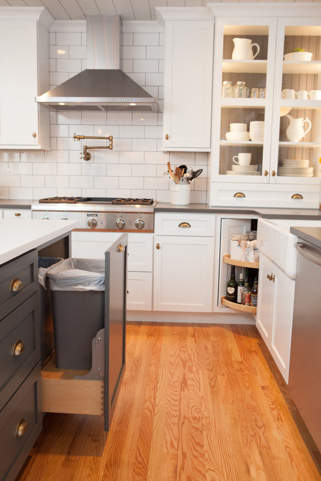 Mid-sized transitional u-shaped light wood floor eat-in kitchen photo in Chicago with a farmhouse sink, recessed-panel cabinets, white cabinets, quartz countertops, multicolored backsplash, subway tile backsplash, stainless steel appliances and an island