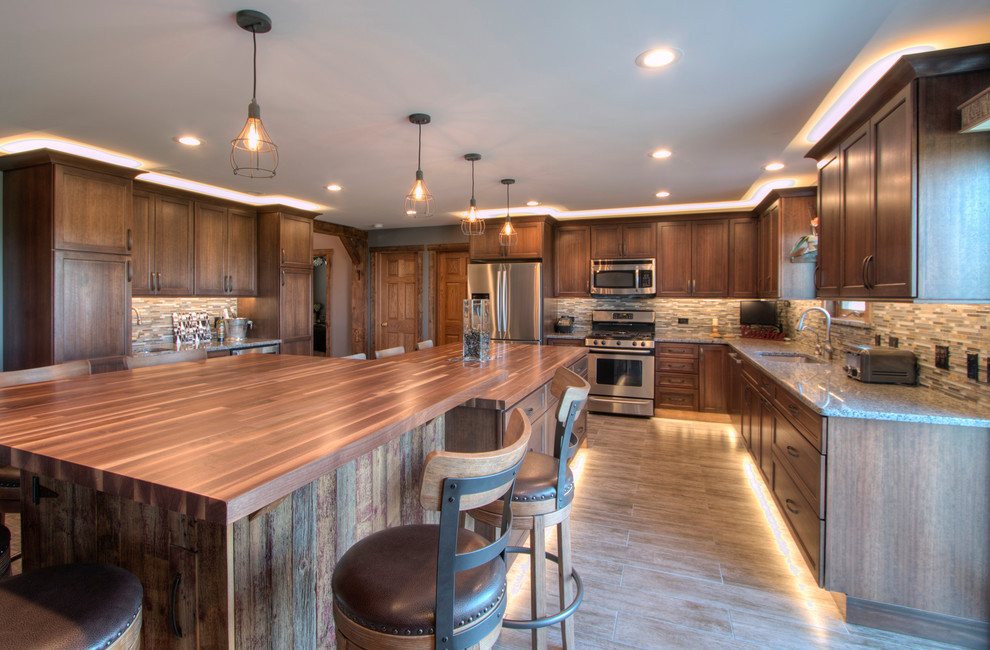 Large rustic l-shaped kitchen pantry in Milwaukee with a submerged sink, flat-panel cabinets, medium wood cabinets, granite worktops, beige splashback, ceramic splashback, stainless steel appliances, porcelain flooring and an island.