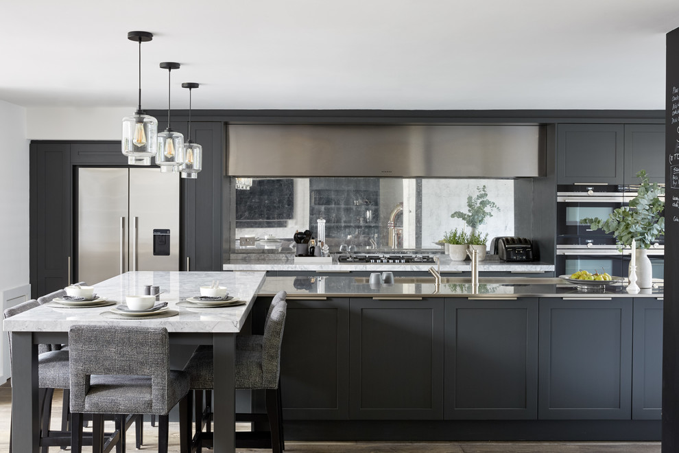 Design ideas for a large contemporary galley open plan kitchen in London with an integrated sink, recessed-panel cabinets, grey cabinets, marble worktops, metallic splashback, mirror splashback, stainless steel appliances, dark hardwood flooring, a breakfast bar, brown floors and white worktops.