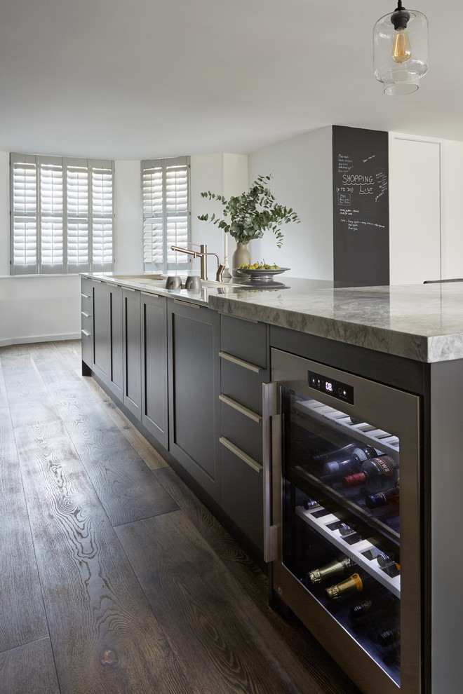 This is an example of a large contemporary galley open plan kitchen in London with an integrated sink, recessed-panel cabinets, grey cabinets, marble worktops, metallic splashback, mirror splashback, stainless steel appliances, dark hardwood flooring, a breakfast bar, brown floors and white worktops.