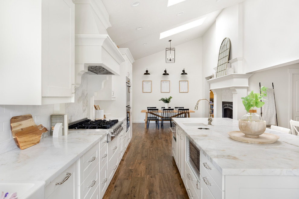 Exempel på ett mellanstort lantligt vit vitt kök, med en rustik diskho, skåp i shakerstil, vita skåp, marmorbänkskiva, vitt stänkskydd, stänkskydd i marmor, rostfria vitvaror, klinkergolv i porslin, en köksö och brunt golv