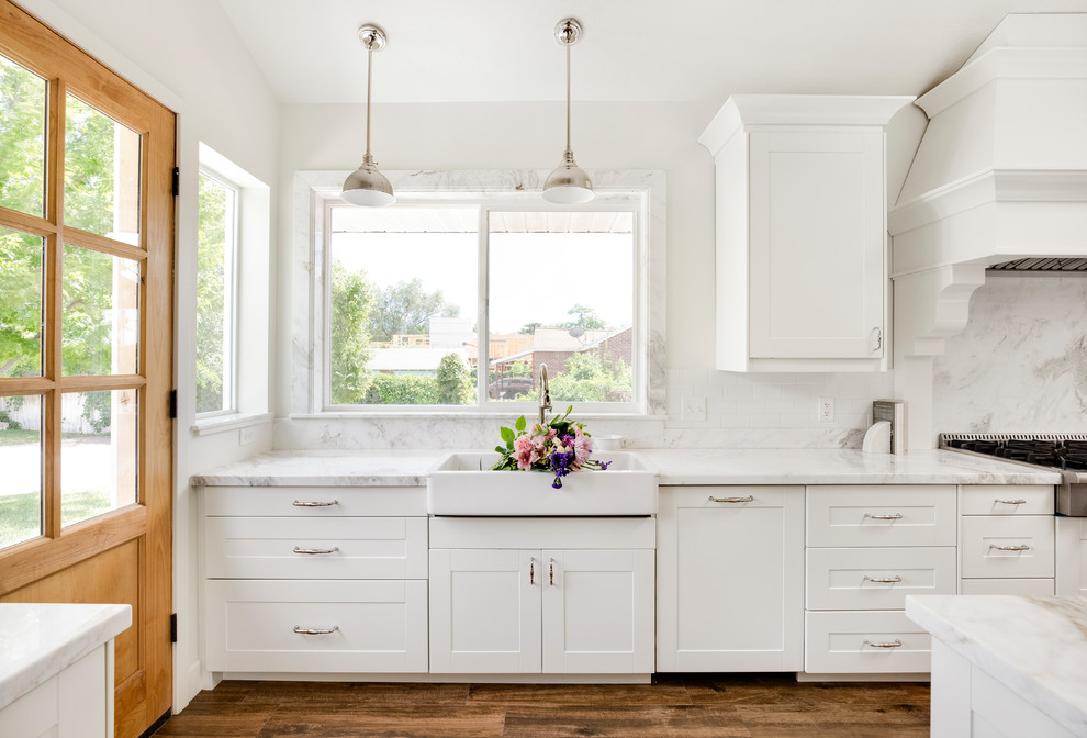 Lantlig inredning av ett mellanstort vit vitt kök, med en rustik diskho, skåp i shakerstil, vita skåp, marmorbänkskiva, vitt stänkskydd, stänkskydd i marmor, rostfria vitvaror, klinkergolv i porslin, en köksö och brunt golv
