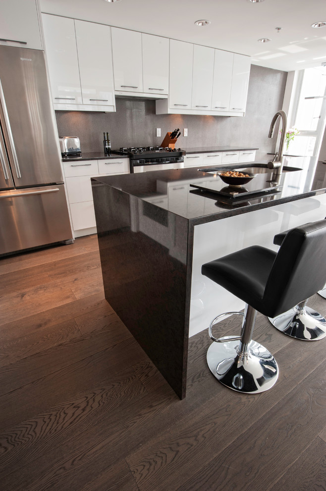 Trendy galley gray floor kitchen photo in Vancouver with a double-bowl sink, flat-panel cabinets, white cabinets, quartz countertops, gray backsplash, stainless steel appliances, an island and black countertops