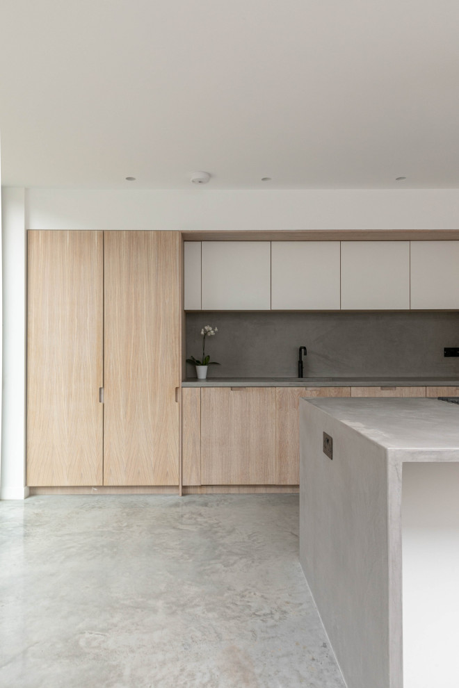 Пример оригинального дизайна: параллельная кухня-гостиная среднего размера в стиле модернизм с плоскими фасадами, светлыми деревянными фасадами, столешницей из бетона, островом и серой столешницей