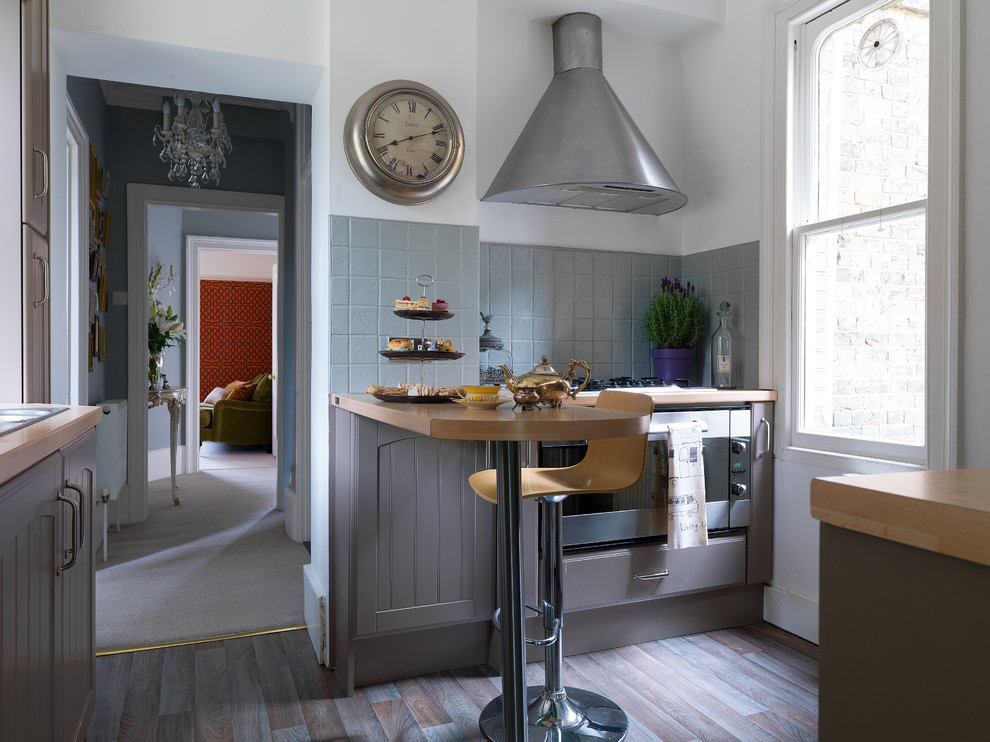 Klassisk inredning av ett litet kök, med grå skåp, träbänkskiva, grått stänkskydd, rostfria vitvaror, en halv köksö och flerfärgat golv