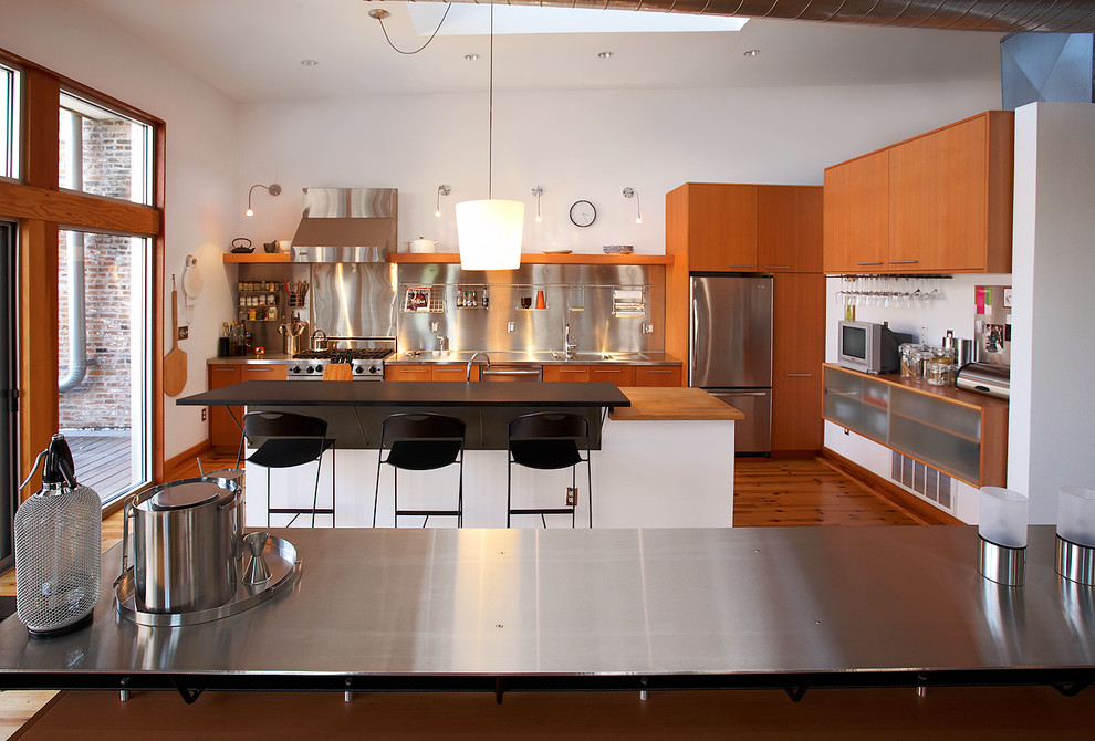Inspiration for a mid-sized industrial l-shaped light wood floor eat-in kitchen remodel in St Louis with flat-panel cabinets, medium tone wood cabinets, metallic backsplash, stainless steel appliances, wood countertops, an island, a drop-in sink and metal backsplash