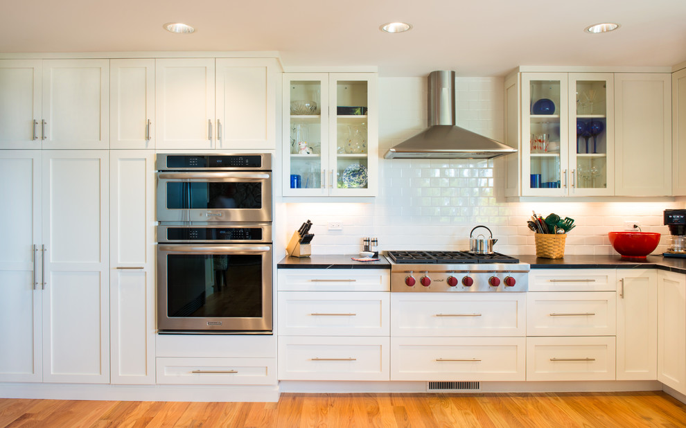 Exempel på ett modernt kök, med en undermonterad diskho, luckor med glaspanel, bänkskiva i täljsten, vitt stänkskydd, stänkskydd i keramik, rostfria vitvaror och ljust trägolv