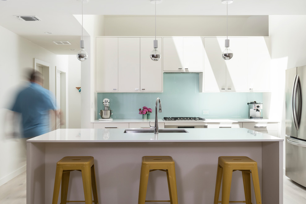 Immagine di una cucina minimalista di medie dimensioni con lavello sottopiano, ante lisce, ante bianche, top in quarzo composito, paraspruzzi blu, paraspruzzi con lastra di vetro, elettrodomestici in acciaio inossidabile, parquet chiaro e pavimento bianco