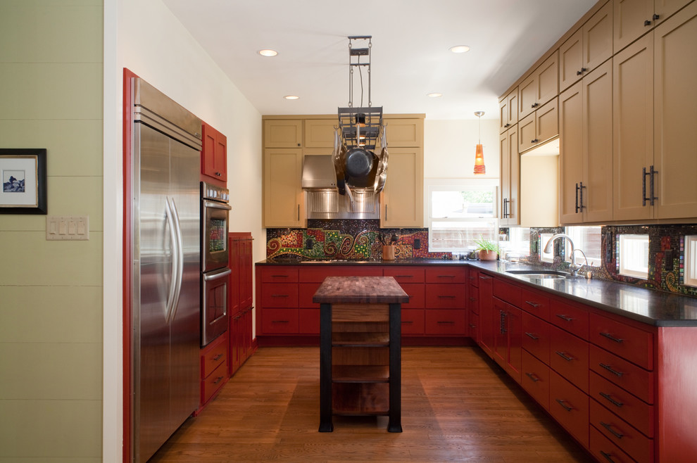 На фото: п-образная, отдельная кухня в современном стиле с техникой из нержавеющей стали, красными фасадами, фасадами в стиле шейкер и разноцветным фартуком