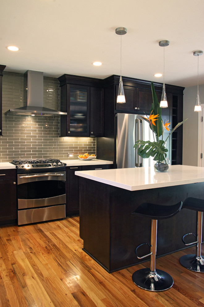 Foto på ett mellanstort vintage vit kök, med skåp i shakerstil, svarta skåp, bänkskiva i kvarts, grönt stänkskydd, stänkskydd i glaskakel, rostfria vitvaror, ljust trägolv, en köksö och brunt golv