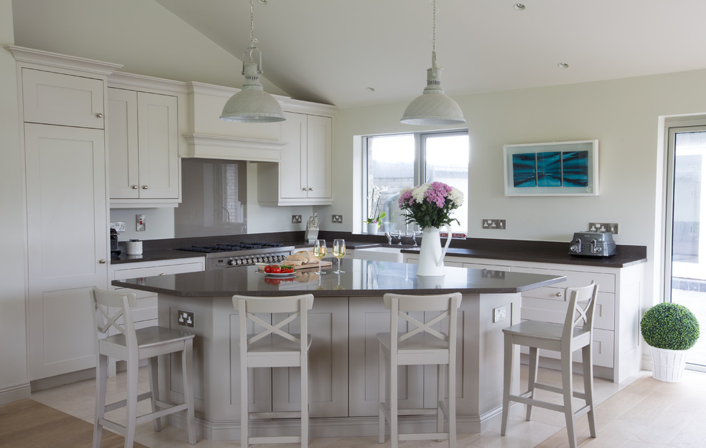 This is an example of a medium sized nautical l-shaped open plan kitchen in Dublin with a belfast sink, shaker cabinets, beige cabinets, quartz worktops, brown splashback, glass sheet splashback, stainless steel appliances and an island.