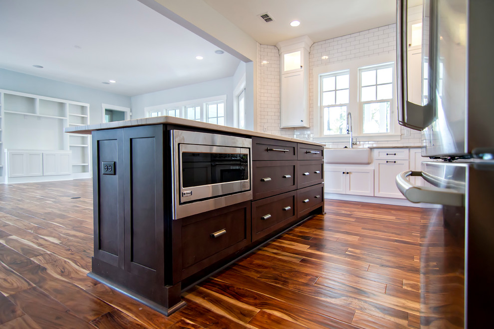 Inspiration for a coastal l-shaped medium tone wood floor eat-in kitchen remodel in Jacksonville with an undermount sink, flat-panel cabinets, white cabinets, granite countertops, white backsplash, subway tile backsplash, stainless steel appliances and an island