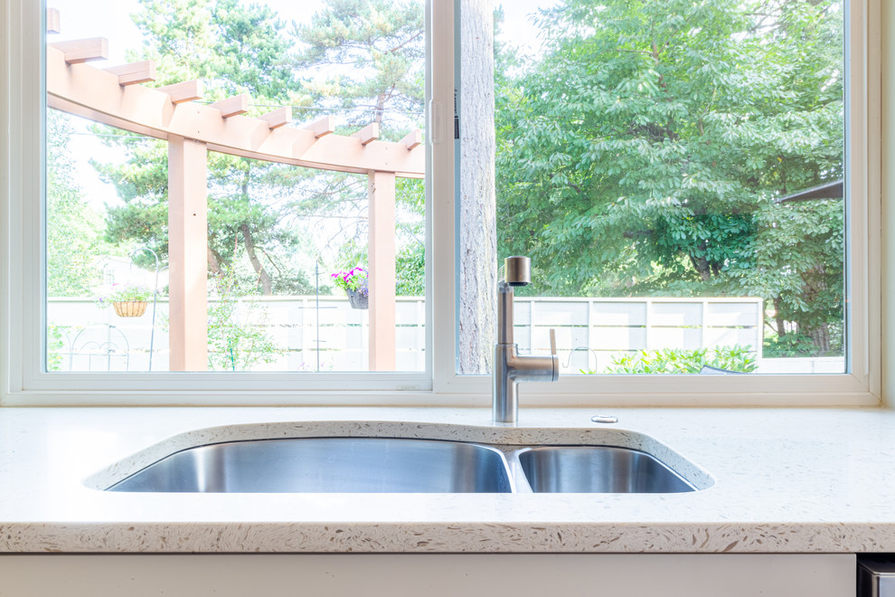 Inspiration for a medium sized contemporary l-shaped open plan kitchen in Portland with a double-bowl sink, shaker cabinets, white cabinets, engineered stone countertops, white splashback, ceramic splashback, stainless steel appliances, medium hardwood flooring, an island and white worktops.