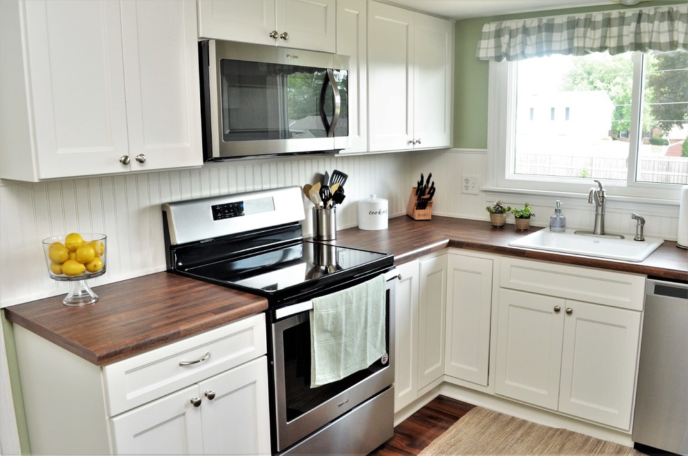 Bild på ett mellanstort lantligt brun brunt kök, med en nedsänkt diskho, skåp i shakerstil, vita skåp, laminatbänkskiva, vitt stänkskydd, stänkskydd i trä, rostfria vitvaror, en halv köksö och brunt golv