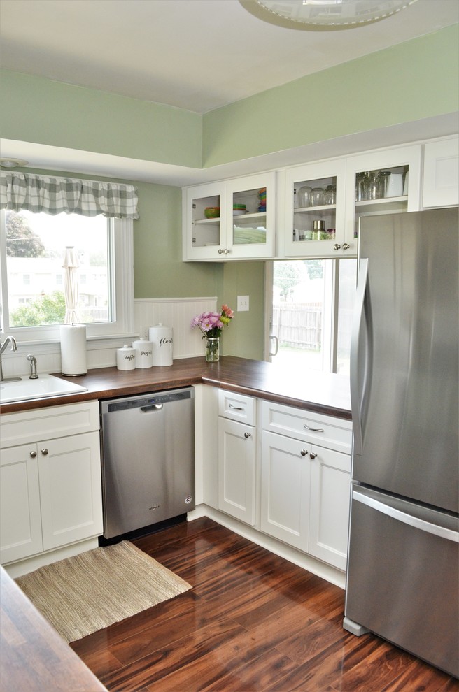 Lantlig inredning av ett mellanstort brun brunt kök, med en nedsänkt diskho, skåp i shakerstil, vita skåp, laminatbänkskiva, vitt stänkskydd, stänkskydd i trä, rostfria vitvaror, en halv köksö och brunt golv