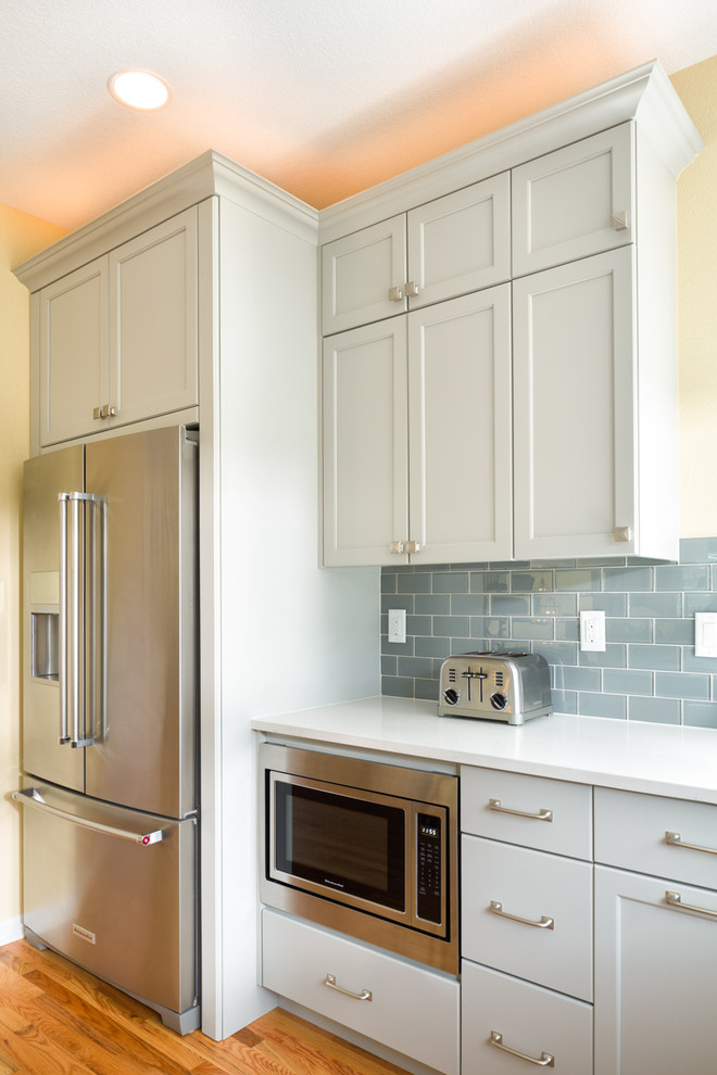 Inredning av ett klassiskt mellanstort kök, med en undermonterad diskho, luckor med infälld panel, grå skåp, bänkskiva i kvarts, blått stänkskydd, stänkskydd i glaskakel, rostfria vitvaror, ljust trägolv och en köksö
