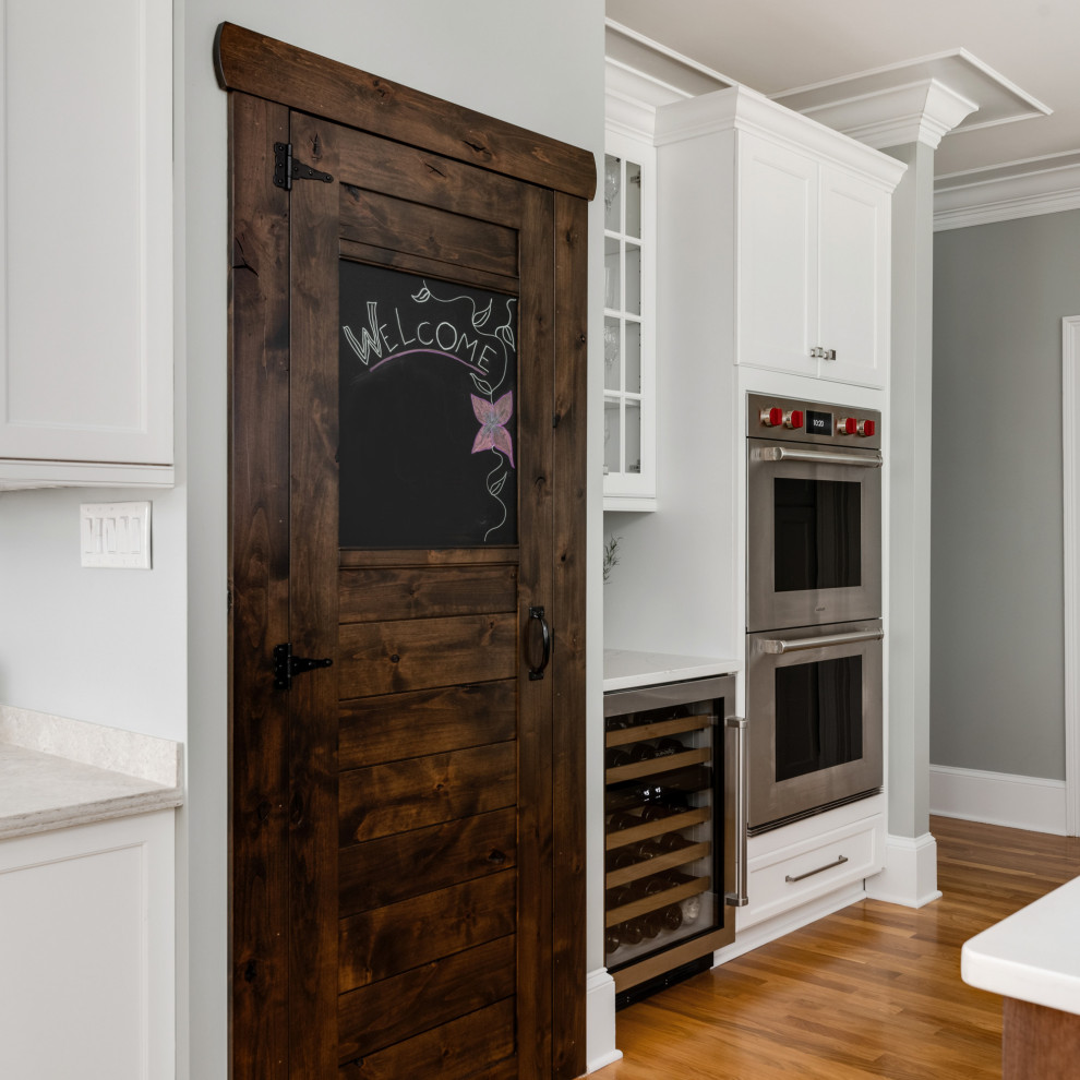 Inspiration for a medium sized classic l-shaped kitchen pantry in Charlotte with a belfast sink, shaker cabinets, white cabinets, engineered stone countertops, brown splashback, porcelain splashback, stainless steel appliances, light hardwood flooring, an island, brown floors and yellow worktops.