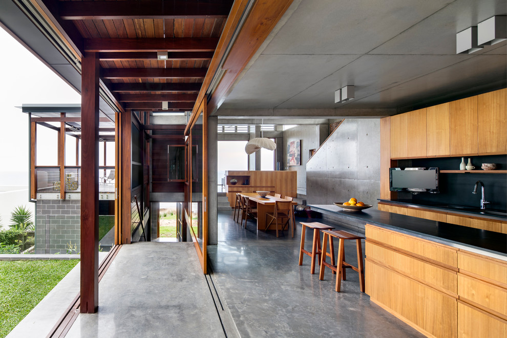 シドニーにあるコンテンポラリースタイルのおしゃれなキッチン (淡色木目調キャビネット、コンクリートの床、アンダーカウンターシンク、フラットパネル扉のキャビネット、黒いキッチンパネル) の写真