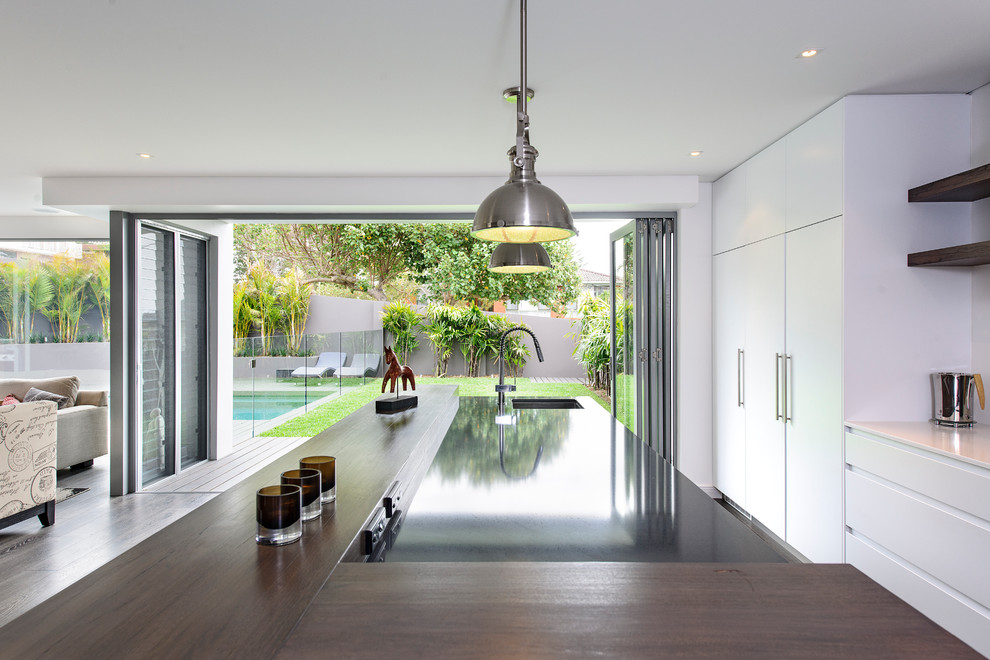 Design ideas for a contemporary galley open plan kitchen in Sydney with a submerged sink, flat-panel cabinets, white cabinets and integrated appliances.