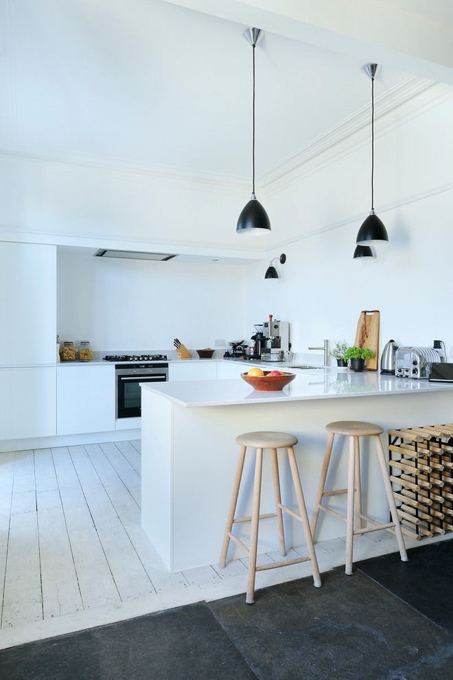 Cette photo montre une cuisine scandinave en U avec un placard à porte plane, des portes de placard blanches, un électroménager en acier inoxydable, parquet clair et une péninsule.