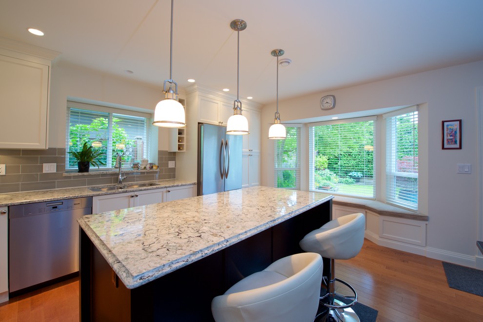 Kitchen - mid-sized traditional u-shaped medium tone wood floor and brown floor kitchen idea in Vancouver with an undermount sink, shaker cabinets, white cabinets, granite countertops, gray backsplash, porcelain backsplash, stainless steel appliances and an island