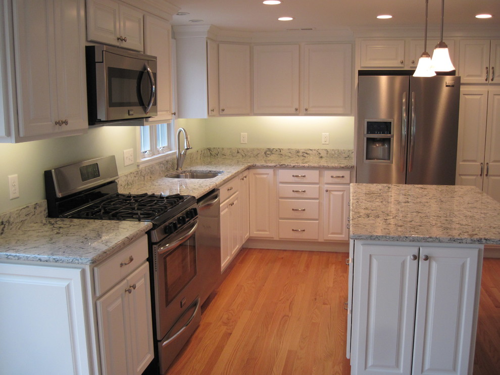 Traditional l-shaped kitchen in Boston with a submerged sink, raised-panel cabinets, white cabinets, engineered stone countertops, stainless steel appliances and light hardwood flooring.