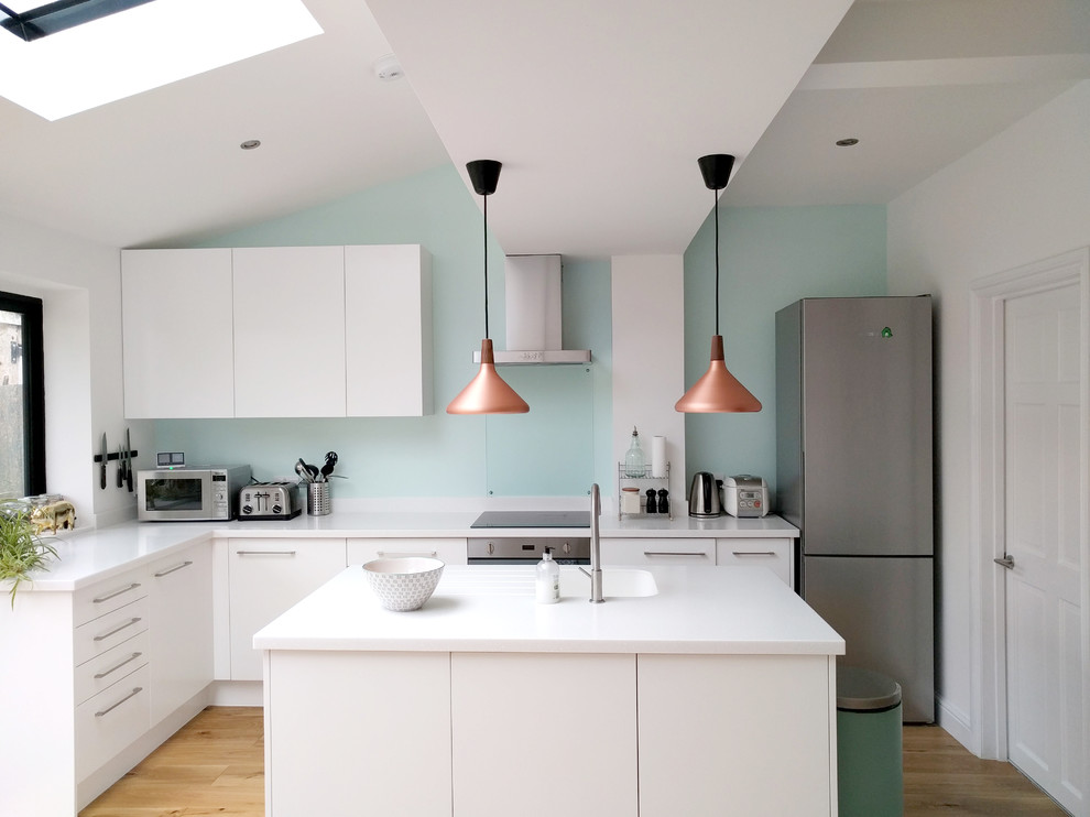 ロンドンにある低価格の中くらいなコンテンポラリースタイルのおしゃれなキッチン (フラットパネル扉のキャビネット、白いキャビネット、人工大理石カウンター、ガラス板のキッチンパネル、白い調理設備、淡色無垢フローリング、一体型シンク、青いキッチンパネル、ベージュの床) の写真
