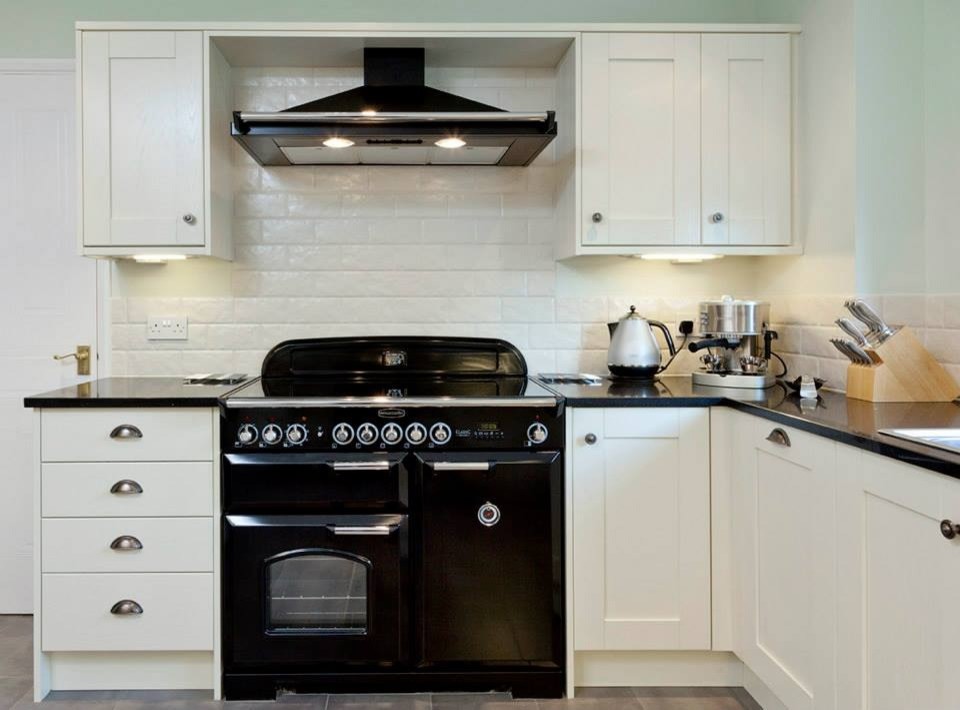 Expansive classic u-shaped enclosed kitchen in Essex with a double-bowl sink, shaker cabinets, beige cabinets, quartz worktops, beige splashback, cement tile splashback, black appliances and porcelain flooring.