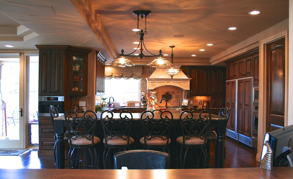 Bild på ett vintage u-kök, med en undermonterad diskho, luckor med upphöjd panel, skåp i mörkt trä, granitbänkskiva, beige stänkskydd, stänkskydd i stenkakel, rostfria vitvaror, mörkt trägolv och en köksö