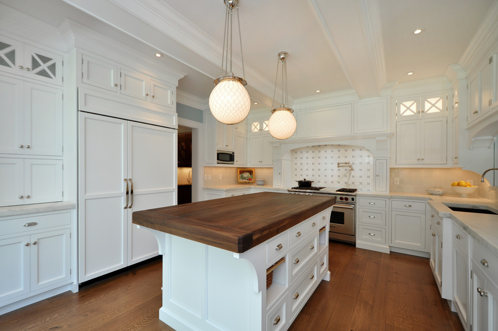 Example of a large trendy u-shaped medium tone wood floor and brown floor eat-in kitchen design in New York with paneled appliances, wood countertops, white cabinets, beige backsplash, an undermount sink, shaker cabinets, ceramic backsplash and an island