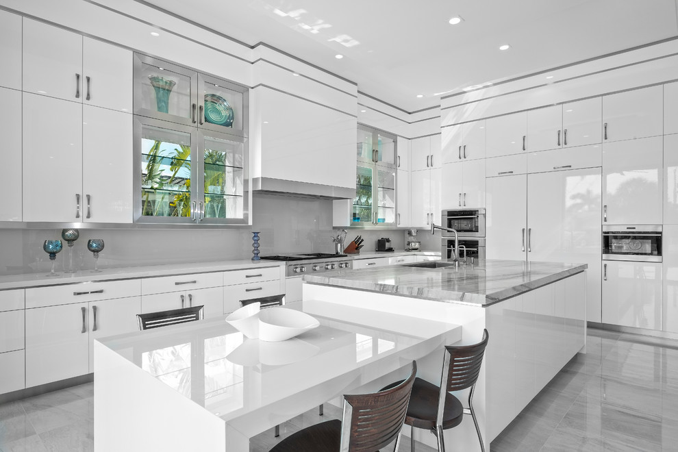Große Moderne Küchenbar in L-Form mit flächenbündigen Schrankfronten, weißen Schränken, Unterbauwaschbecken, Küchenrückwand in Grau, Glasrückwand, Küchengeräten aus Edelstahl, zwei Kücheninseln, grauem Boden und weißer Arbeitsplatte in Miami