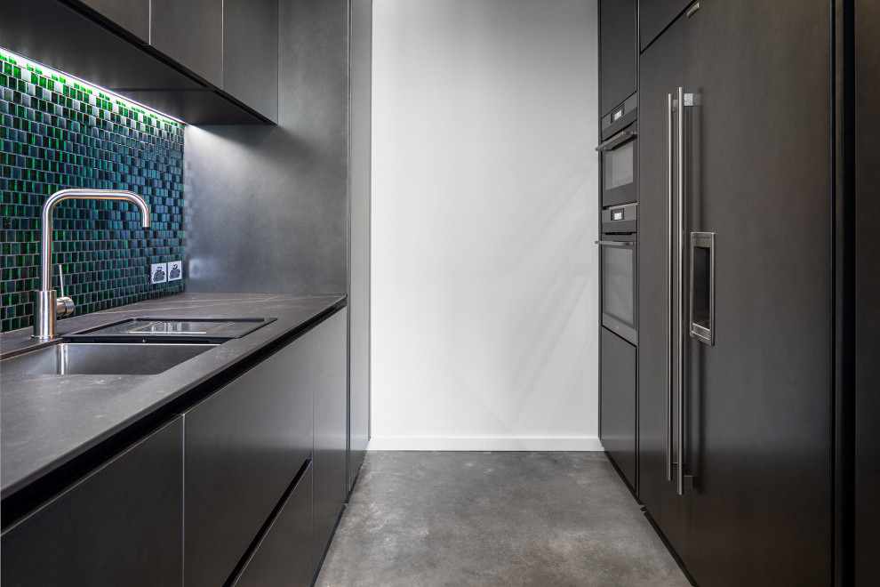 Bild på ett stort eklektiskt grå grått kök med öppen planlösning, med en undermonterad diskho, grönt stänkskydd, stänkskydd i glaskakel, integrerade vitvaror, betonggolv och en köksö