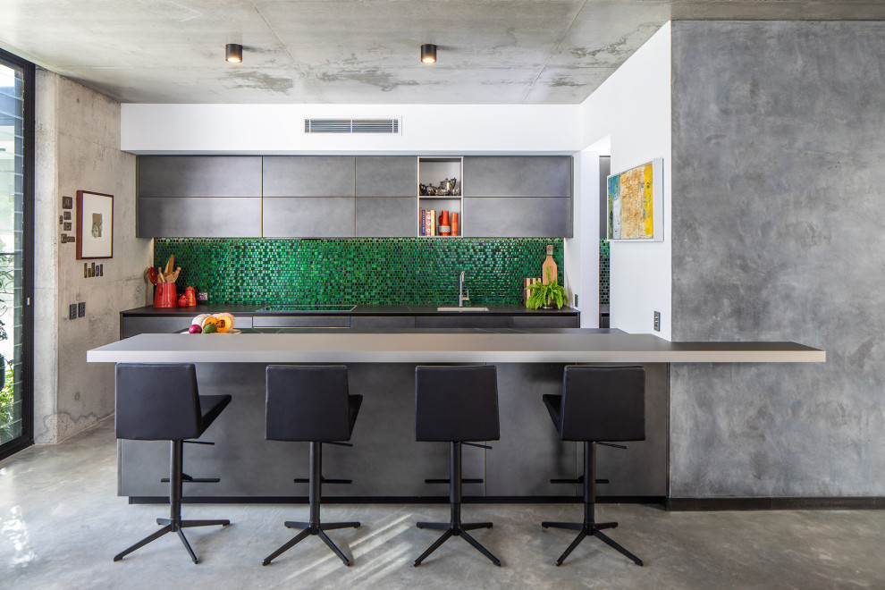 Bild på ett stort funkis grå grått kök med öppen planlösning, med en undermonterad diskho, grönt stänkskydd, stänkskydd i glaskakel, integrerade vitvaror, betonggolv och en köksö