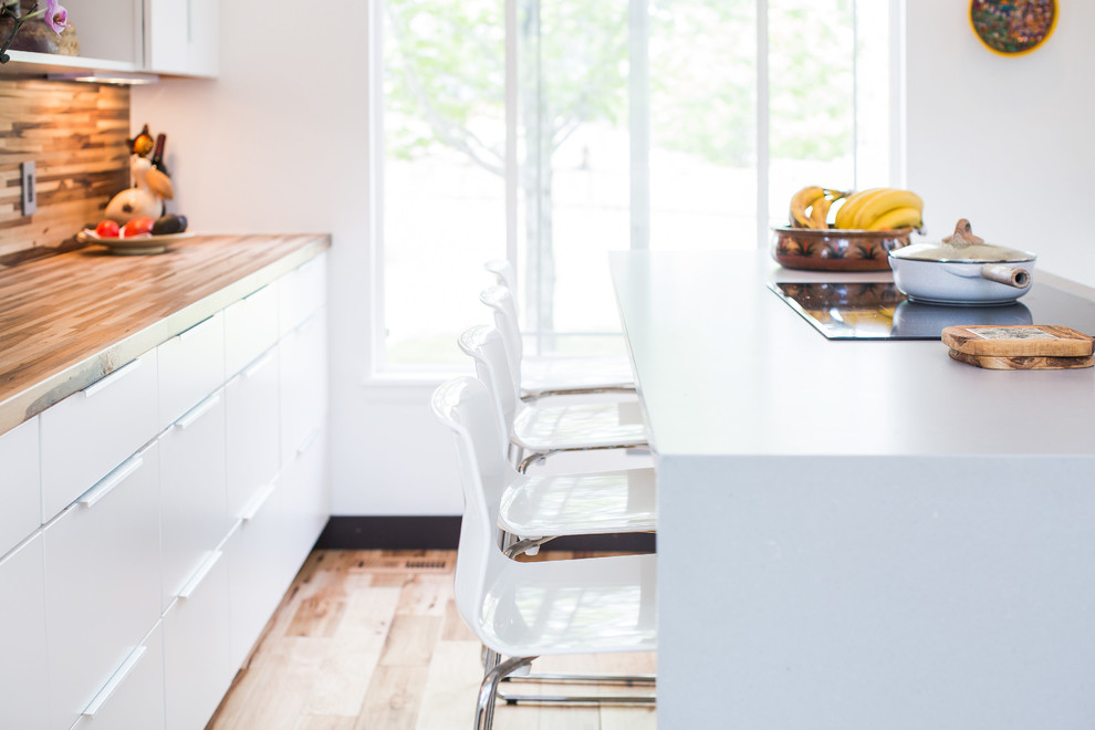 Bild på ett mellanstort funkis grå grått kök, med en undermonterad diskho, släta luckor, vita skåp, bänkskiva i kvarts, vitt stänkskydd, stänkskydd i keramik, svarta vitvaror, ljust trägolv, en köksö och brunt golv