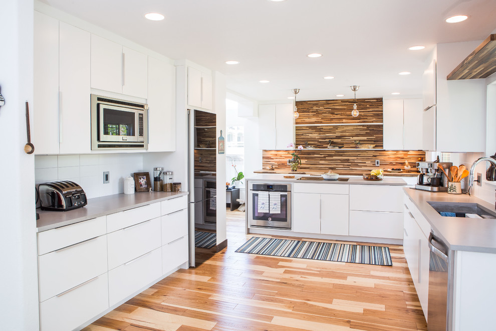 Idéer för att renovera ett mellanstort funkis grå grått kök, med en undermonterad diskho, släta luckor, vita skåp, bänkskiva i kvarts, vitt stänkskydd, stänkskydd i keramik, svarta vitvaror, ljust trägolv, en köksö och brunt golv