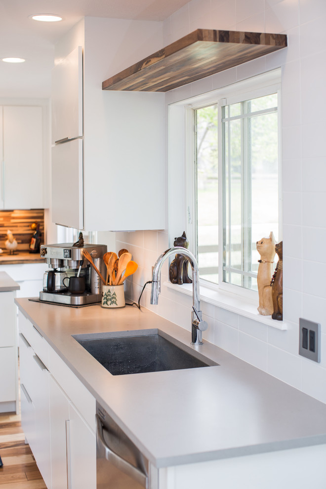 Inredning av ett modernt mellanstort grå grått kök, med en undermonterad diskho, släta luckor, vita skåp, bänkskiva i kvarts, vitt stänkskydd, stänkskydd i keramik, svarta vitvaror, ljust trägolv, en köksö och brunt golv